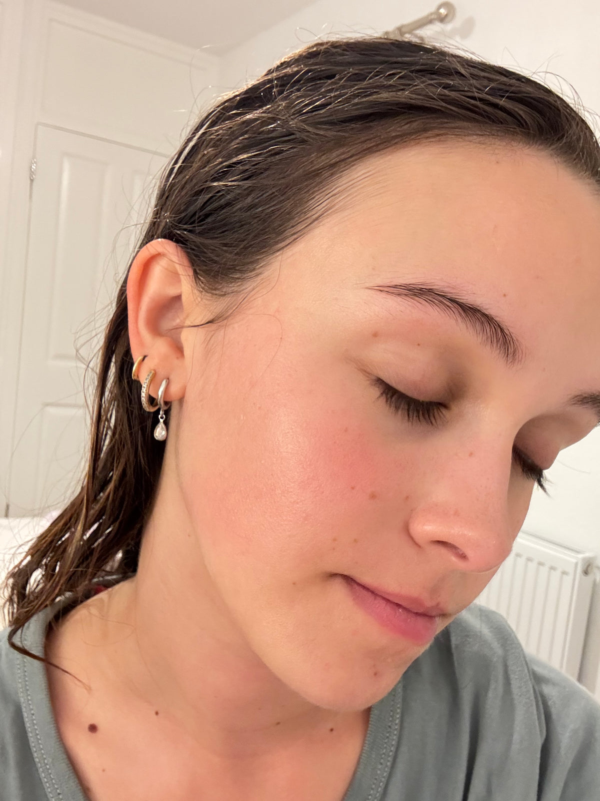A close-up lifestyle shot of a woman with wet hair wearing a stack of three gold hoop earrings, one of which has a small dangling pearl bead.